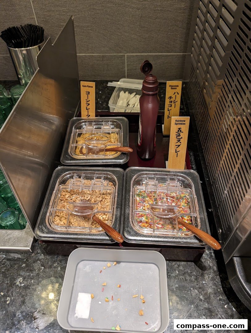 A dessert topping station with corn flakes, chocolate sauce, nuts, and rainbow sprinkles.