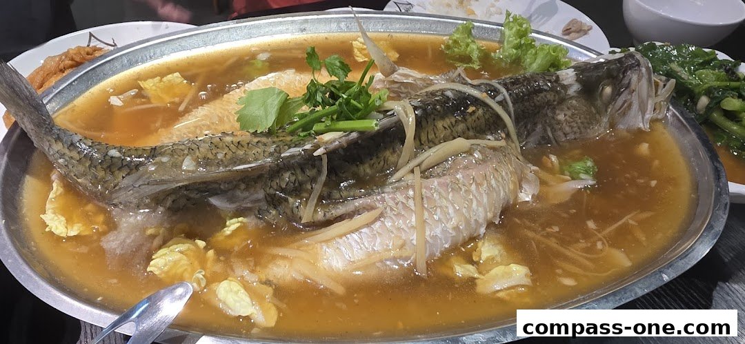 A whole steamed fish in a savory broth with ginger and herbs, served with vegetables.