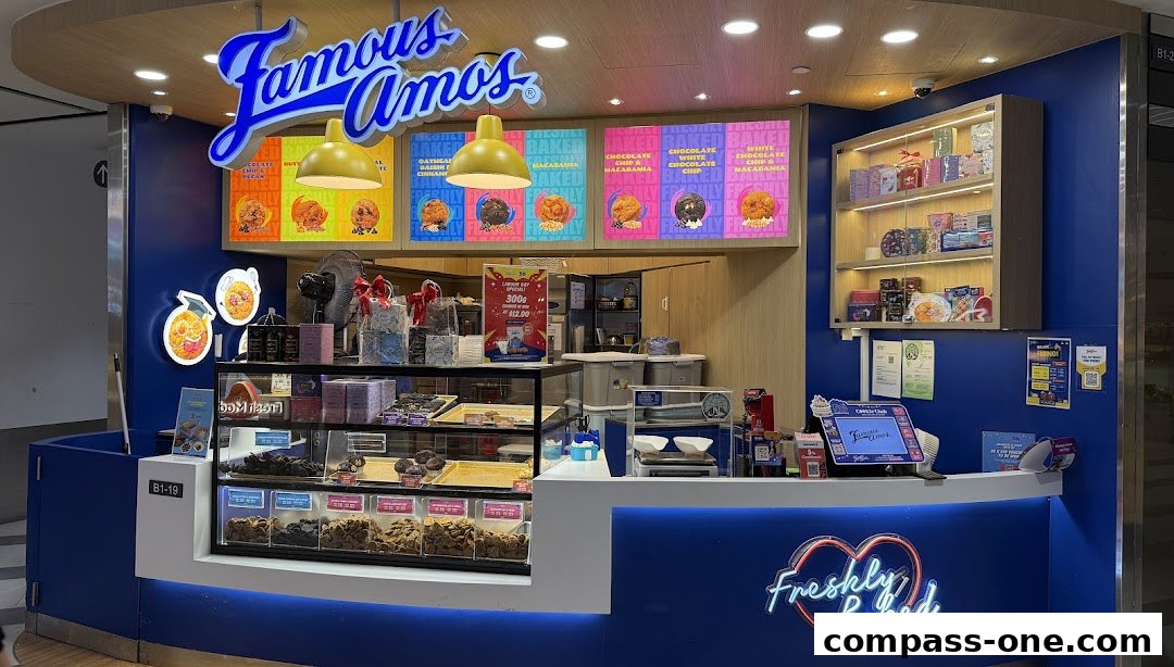 A Famous Amos cookie shop counter with various cookie displays and a 'Freshly Baked' neon sign.