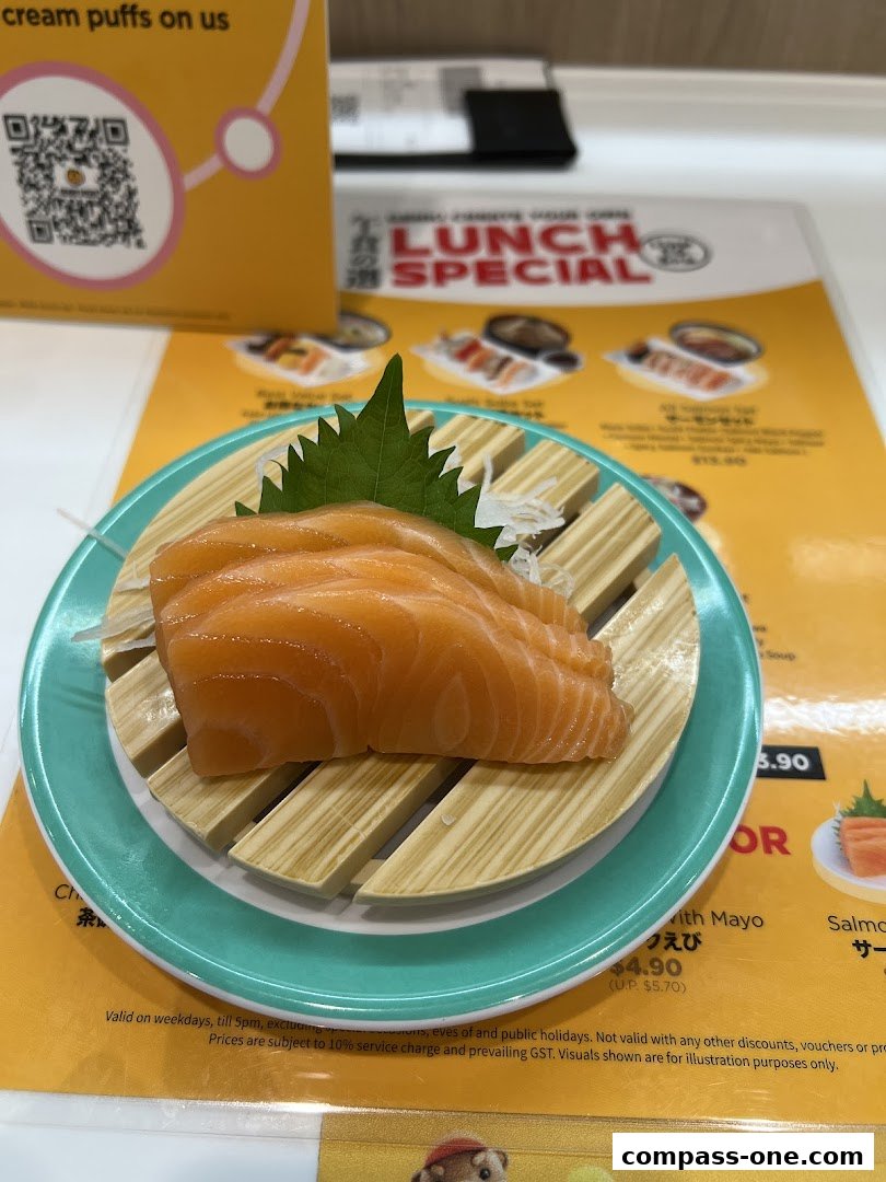 A plate of fresh salmon sashimi served on a bamboo mat with a green leaf garnish.