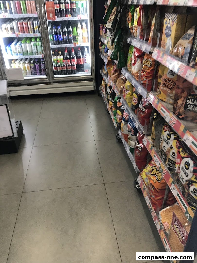 A 7-Eleven store aisle with a refrigerated drinks cooler and shelves stocked with snacks.