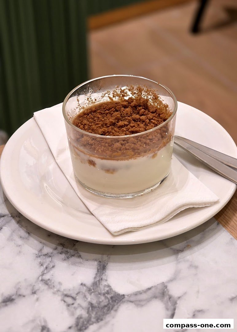 A creamy dessert topped with crushed biscuits served in a glass on a plate.