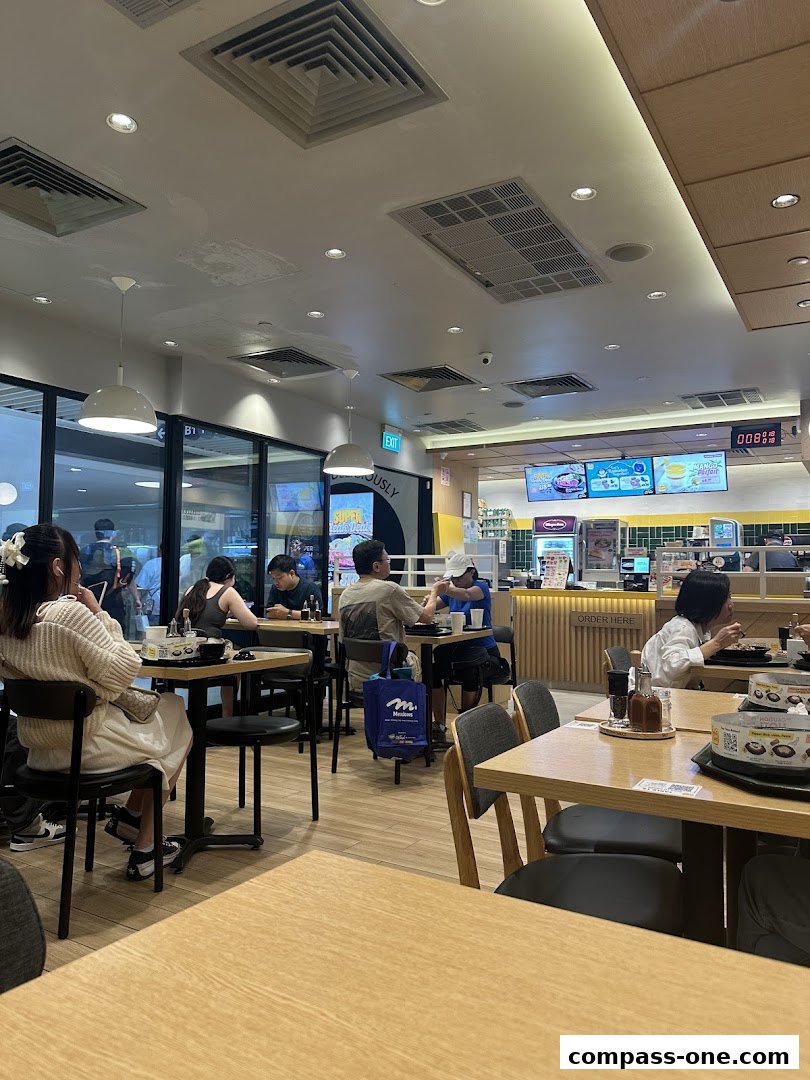 Diners are seated at tables inside a Pepper Lunch restaurant, with a counter and menu displays visible.
