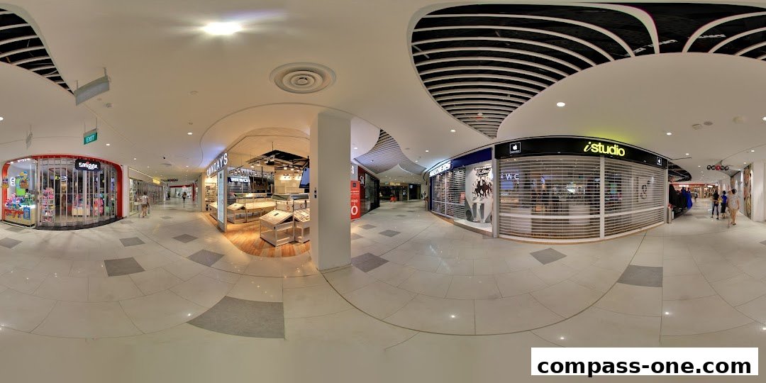 A panoramic view of a shopping mall corridor with various shops including Smiggle, OWNDAYS, and iStudio.