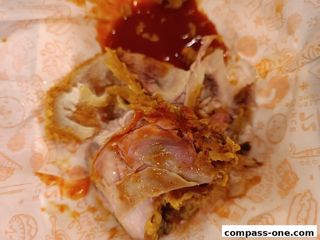 Close-up of Popeyes fried chicken with sauce on branded paper.