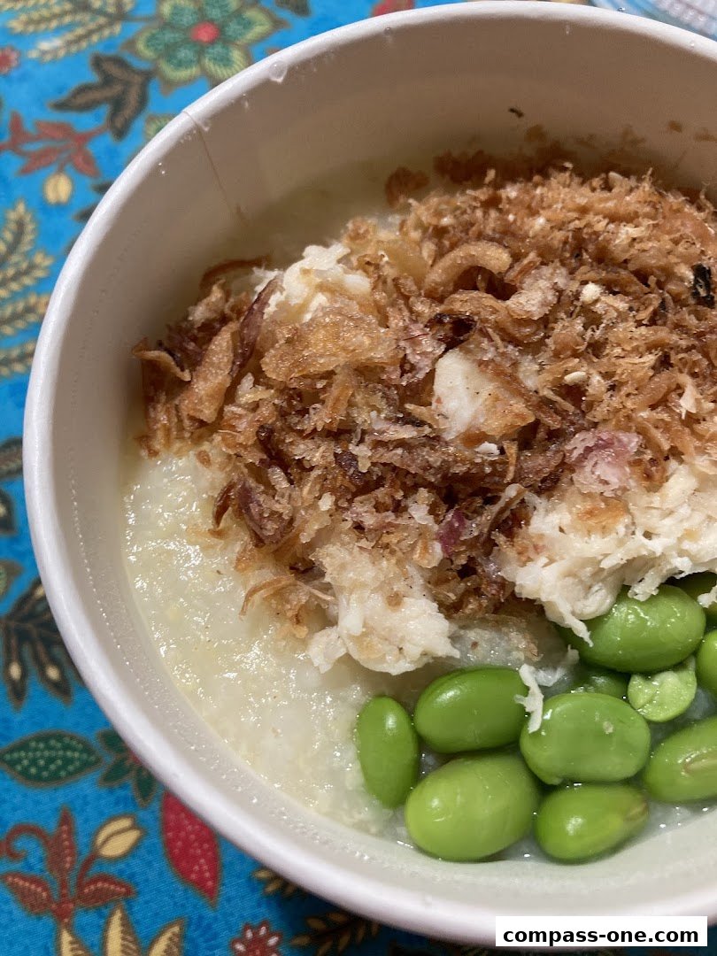 A close-up of a bowl of congee topped with shredded fish, fried shallots, and edamame.
