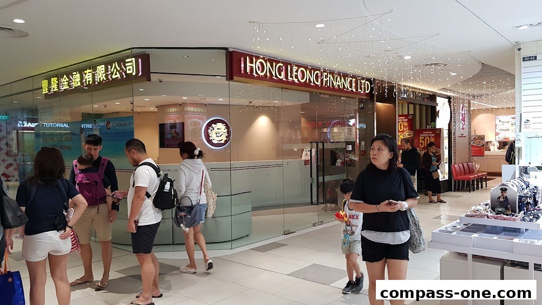 People walking past the Hong Leong Finance Ltd. shop front in a mall.