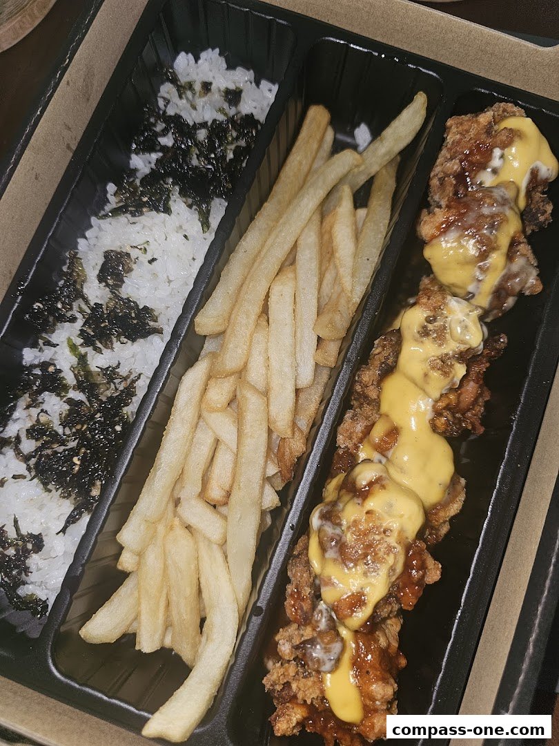 A takeaway box filled with rice, fries, and cheese-drizzled fried chicken.