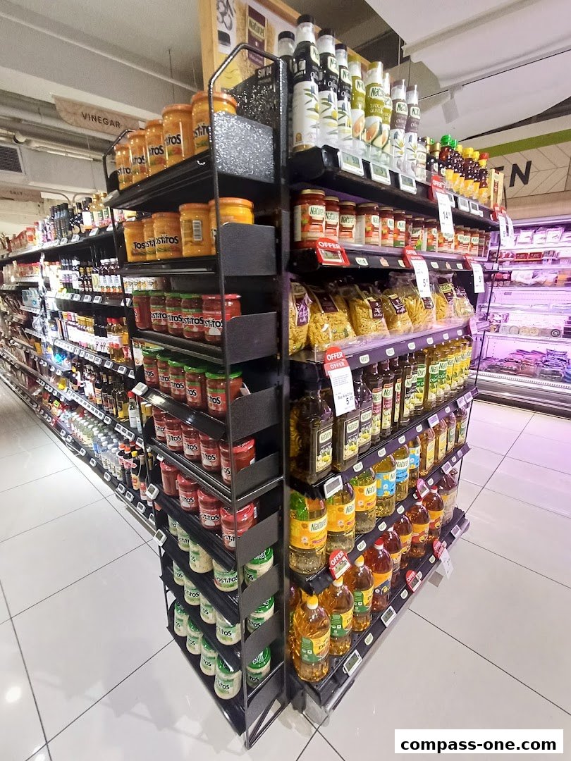 A wide aisle in a supermarket showcasing various food products on shelves, including sauces, oils, and pasta.