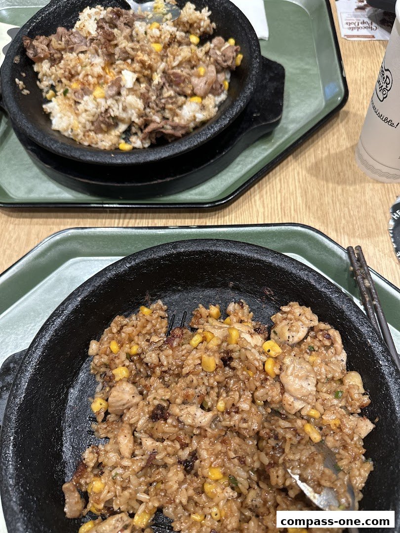 Two sizzling hot plates of rice with meat and corn, served on green trays.