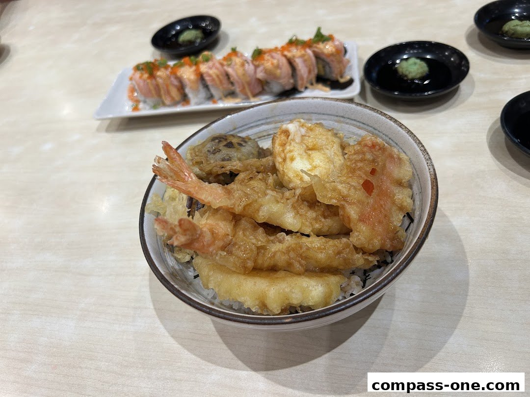 A close-up of a delicious tempura donburi bowl with sushi rolls in the background.