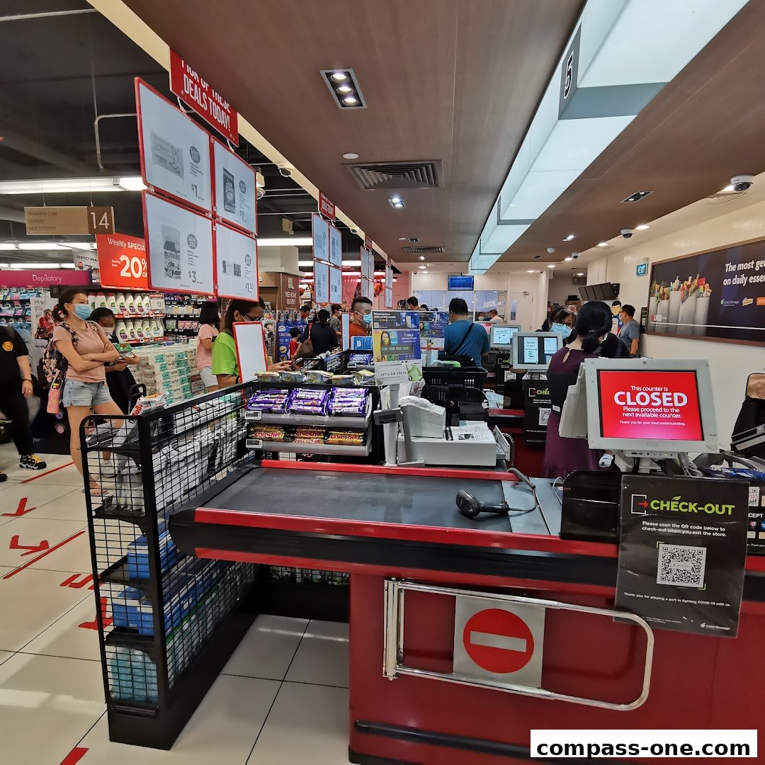 A busy supermarket checkout area with customers and staff, featuring promotional displays and a closed counter.