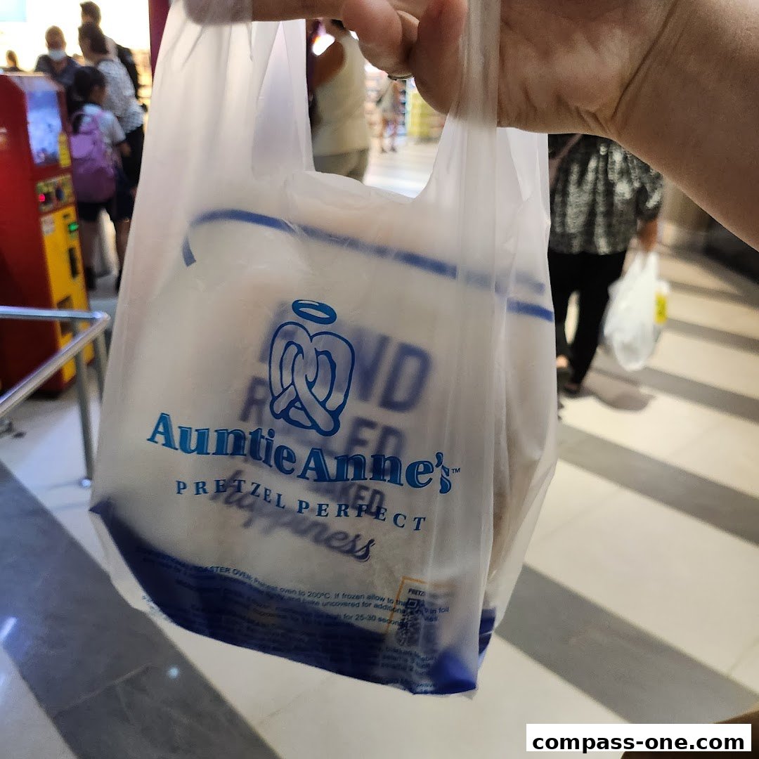 A person holds a plastic bag from Auntie Anne's with pretzels inside.