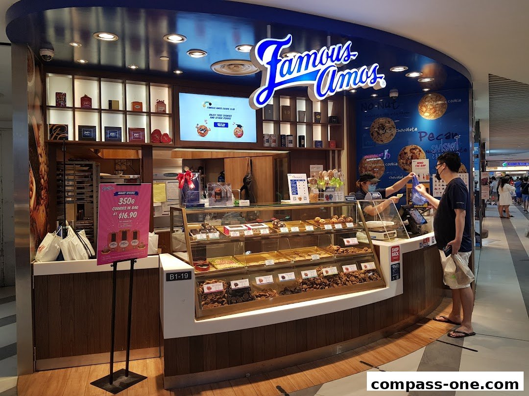 A Famous Amos cookie shop with a display of cookies and a customer being served.