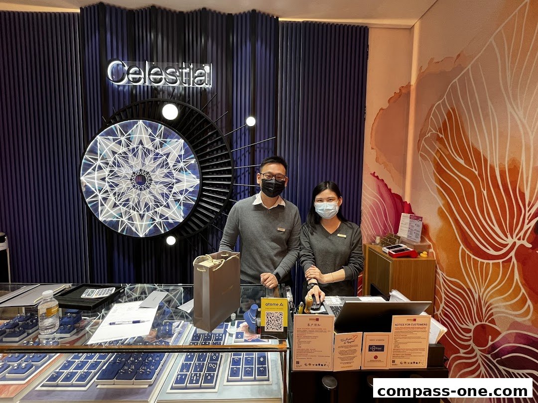 Two staff members stand behind a jewelry counter at Goldheart, with displays of jewelry and a large decorative piece.