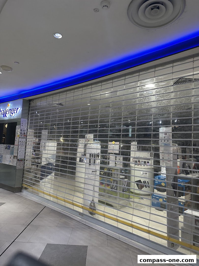 Challenger electronics store with its roller shutter down, displaying various products inside.