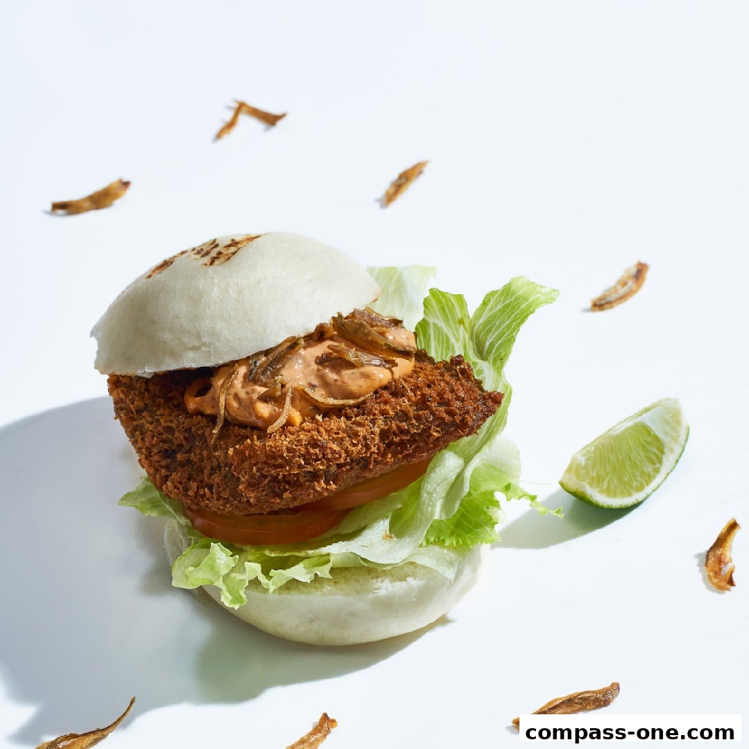 A delicious bao bun burger with crispy fried filling, lettuce, tomato, sauce, and lime.