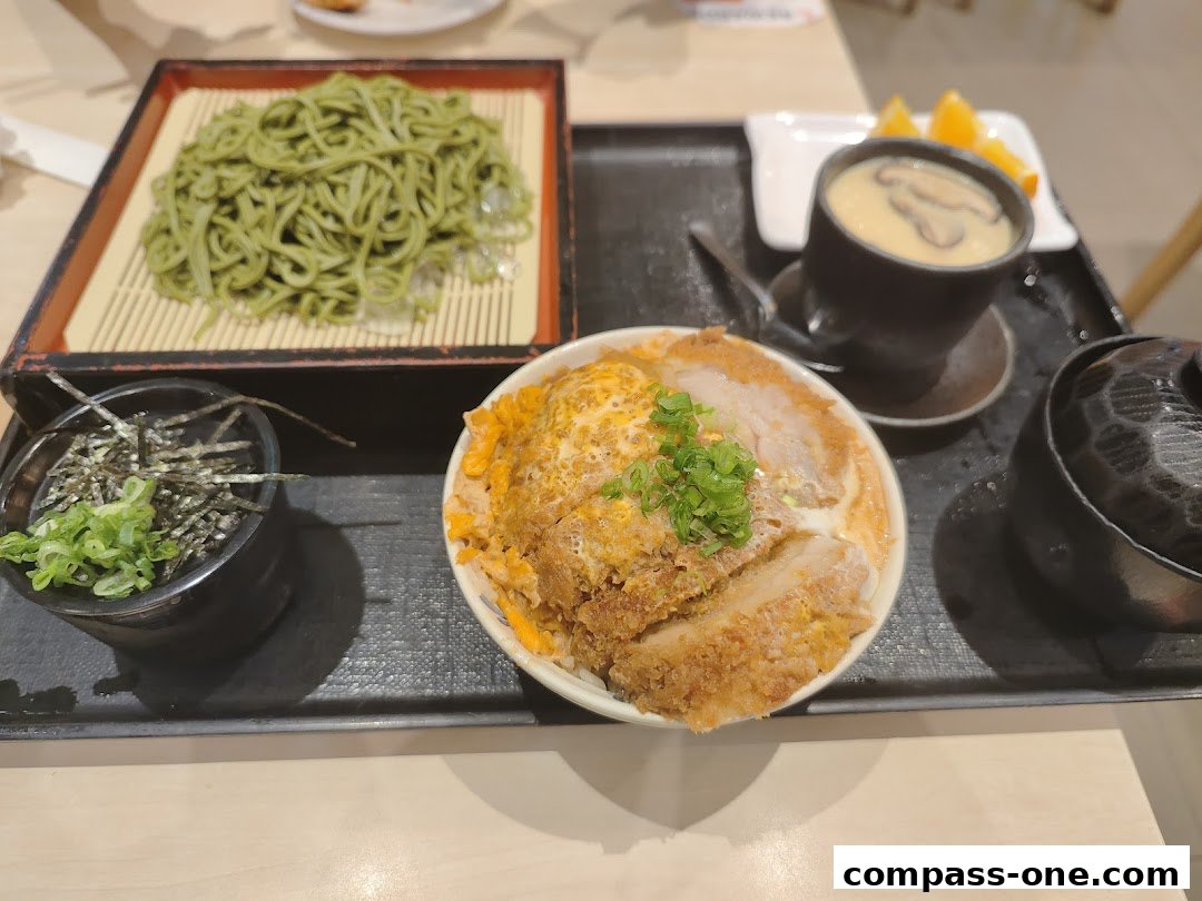 A tray of Japanese food featuring green soba noodles, katsudon, and chawanmushi.