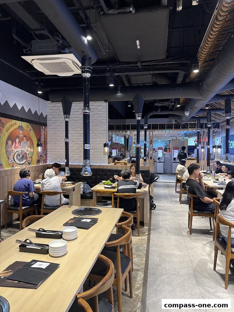 Interior view of a Korean BBQ restaurant with diners seated at tables and ventilation hoods above.