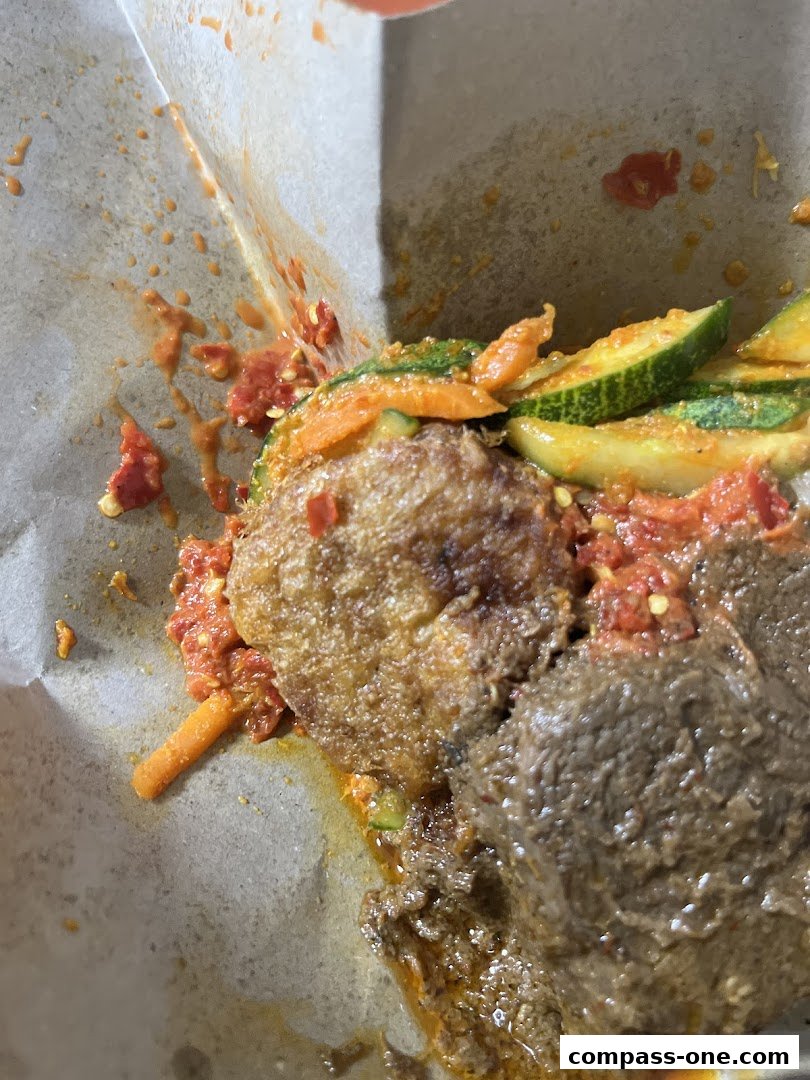 A close-up of a meal with meat, fried item, and vegetables in a paper container.
