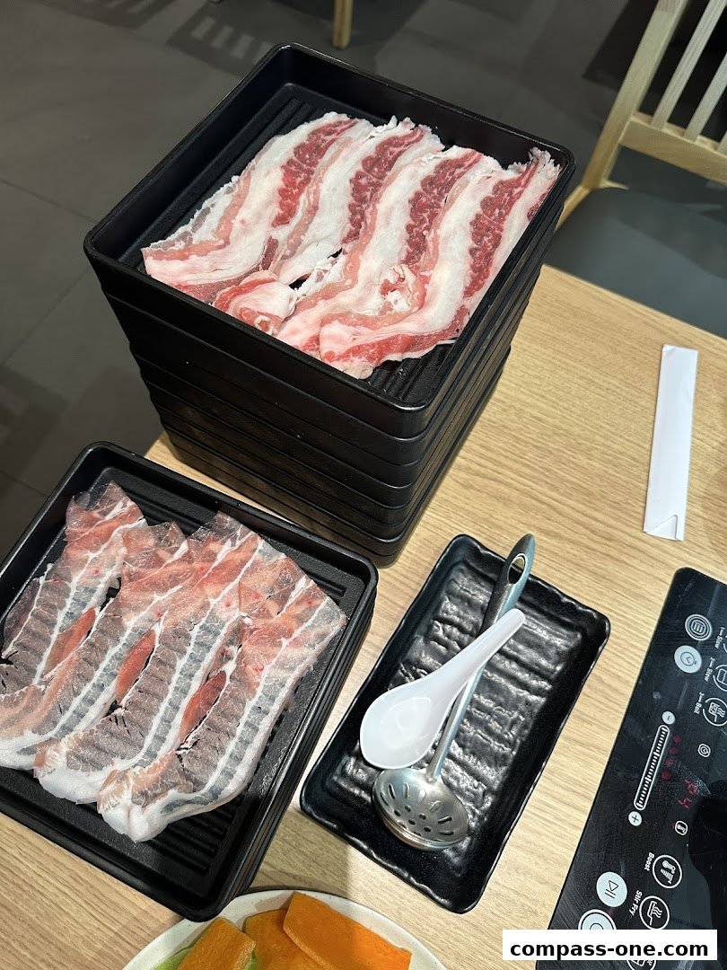 Plates of thinly sliced raw meat, spoons, and a hot pot induction cooker.