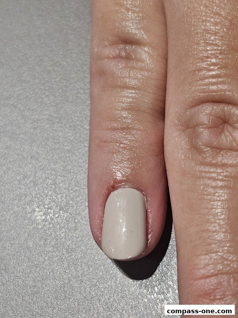 A close-up shot of a person's finger with a freshly painted light beige nail.