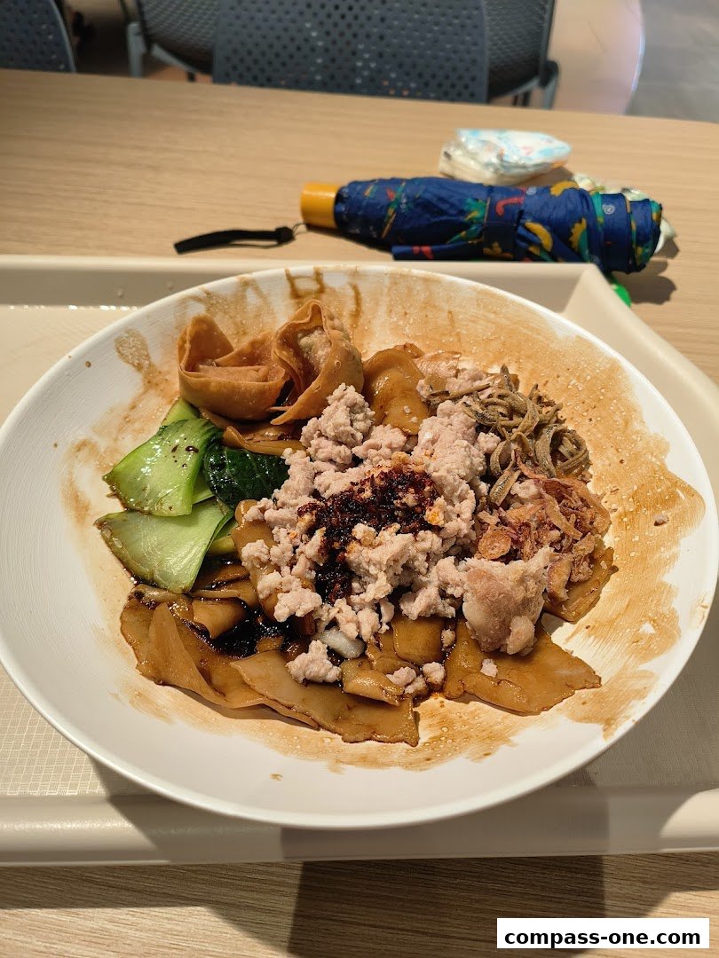 A close-up of a bowl of noodles with minced meat, vegetables, and dumplings.