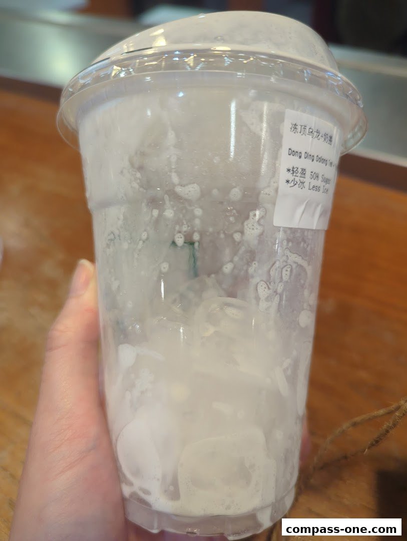 A hand holds a nearly empty plastic cup with ice and foam from a drink.