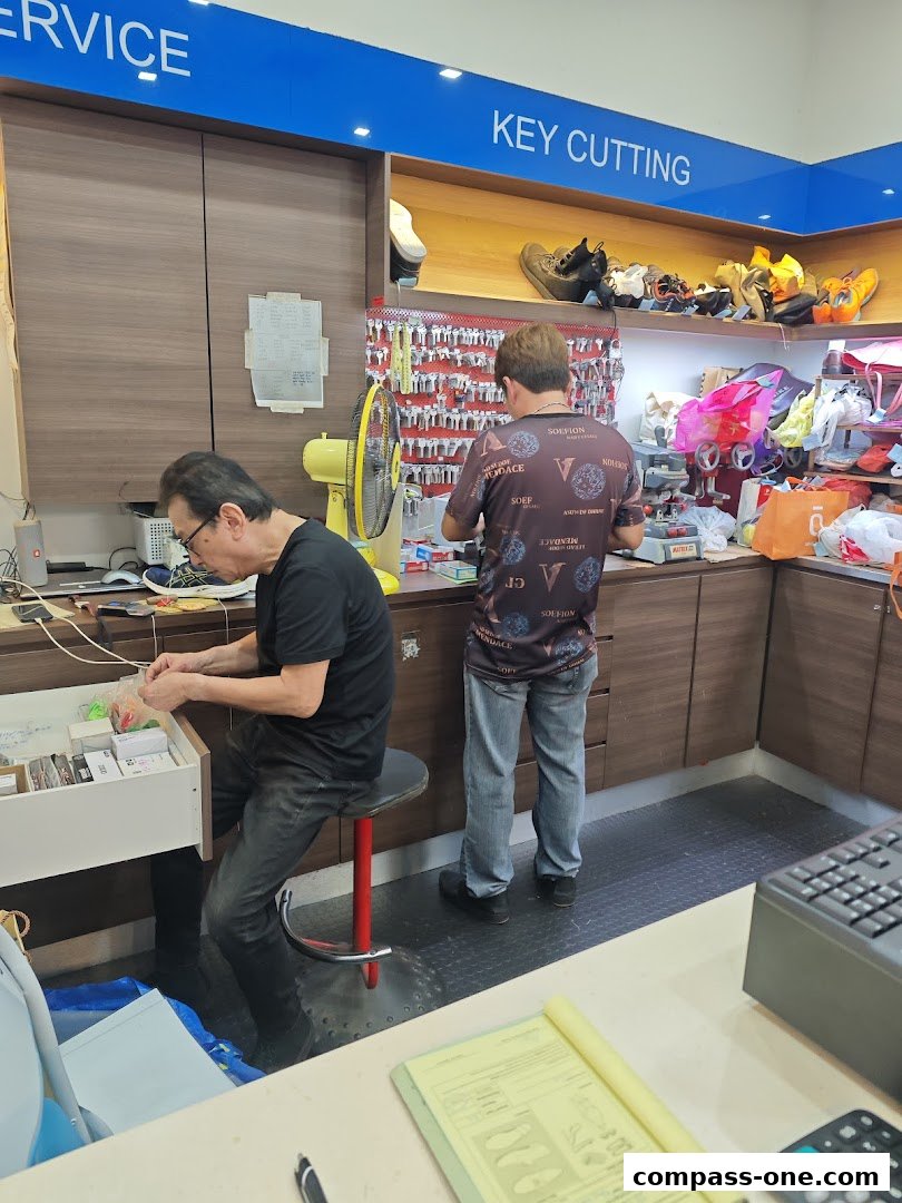 Two men working at a key cutting and shoe repair service counter.