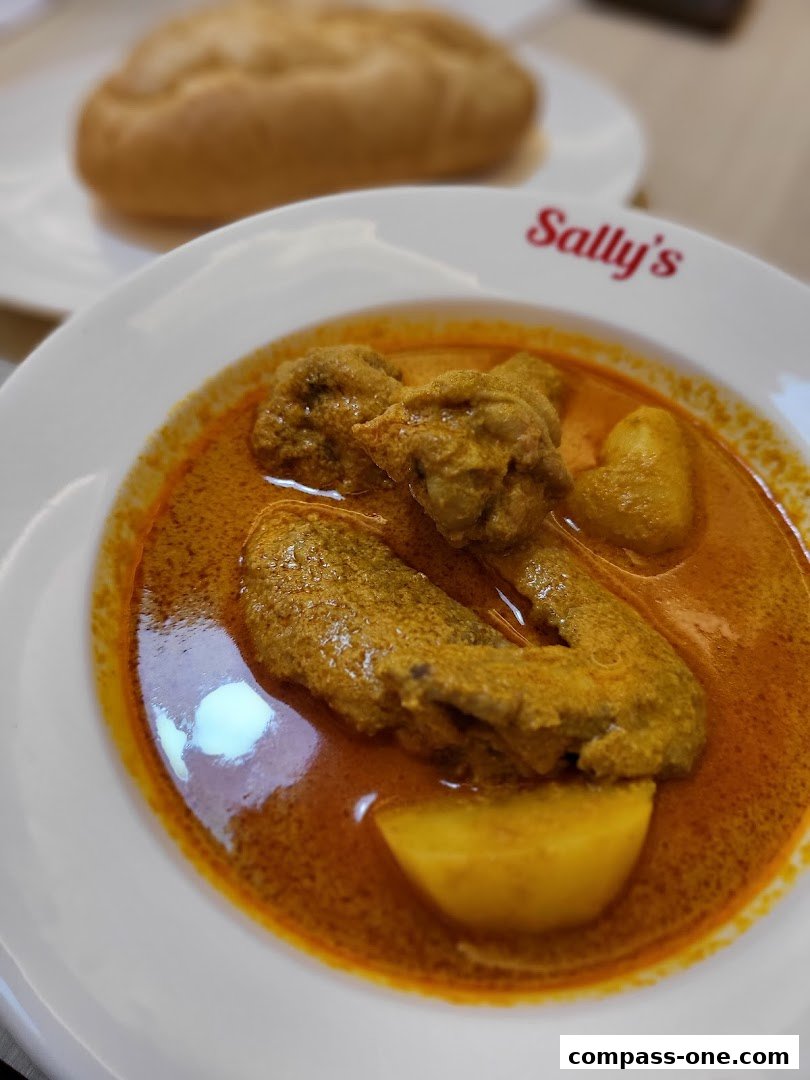 A close-up of a bowl of curry with chicken and potatoes, served with a side of bread.