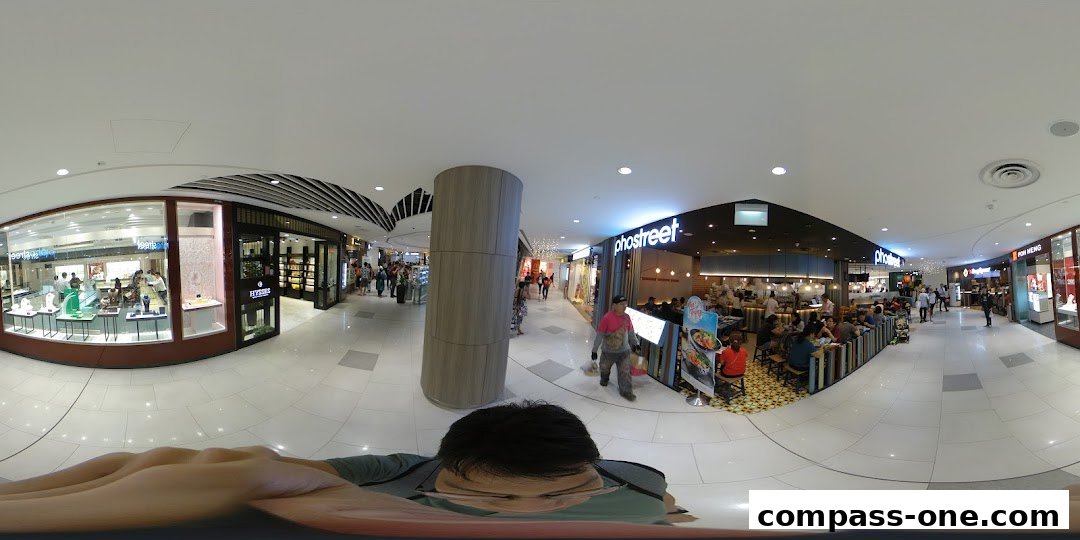 A panoramic view of a shopping mall corridor with shops and diners.