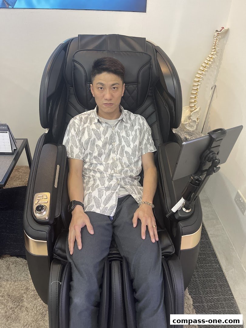 A man sits in a black massage chair with a tablet attached.