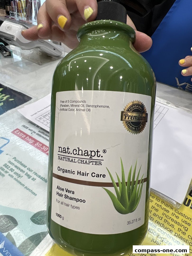 A person holds a large green bottle of Nat. Chapt. Organic Hair Care Aloe Vera Hair Shampoo.