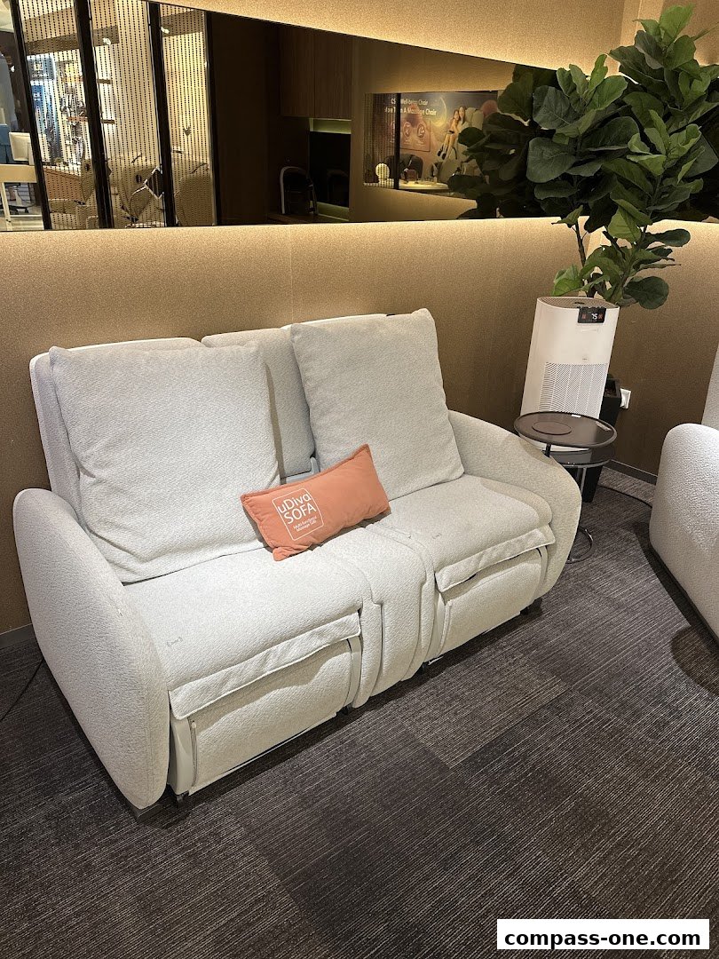 A comfortable white sofa with an orange cushion and a large plant in a modern retail space.