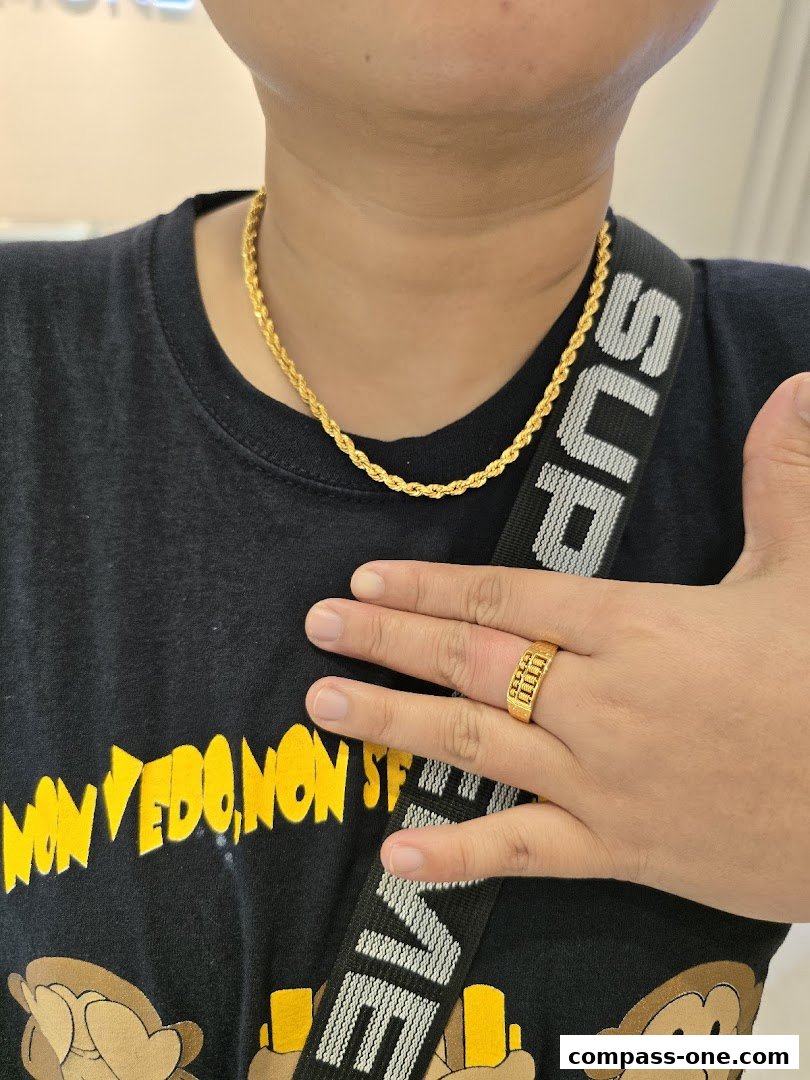 A person wearing a gold rope chain necklace and a gold ring with an abacus design.
