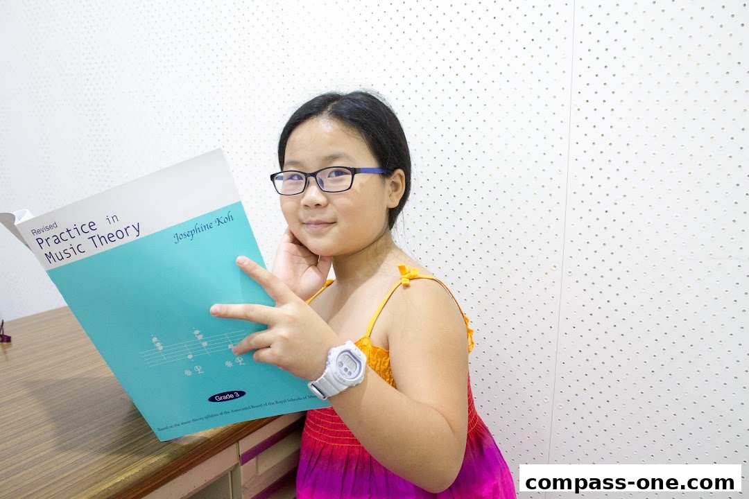 A young girl in glasses holds a music theory practice book, smiling at the camera.