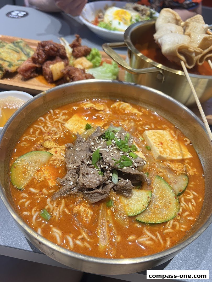 A close-up of a steaming Korean stew with noodles, beef, and vegetables, alongside other Korean dishes.