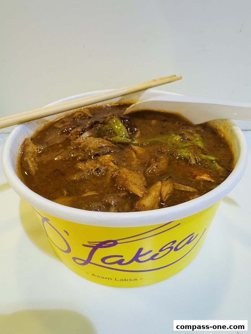 A close-up of a bowl of Asam Laksa with chopsticks and a spoon.
