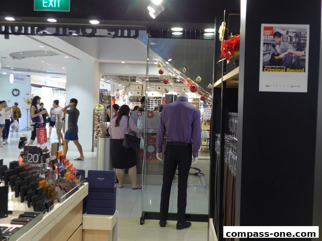 Mannequin in a purple shirt and black pants stands in a retail store with displays of wallets and belts.