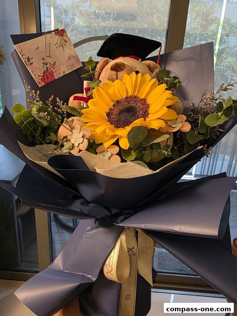 A graduation bouquet featuring a teddy bear, sunflower, and decorative elements.
