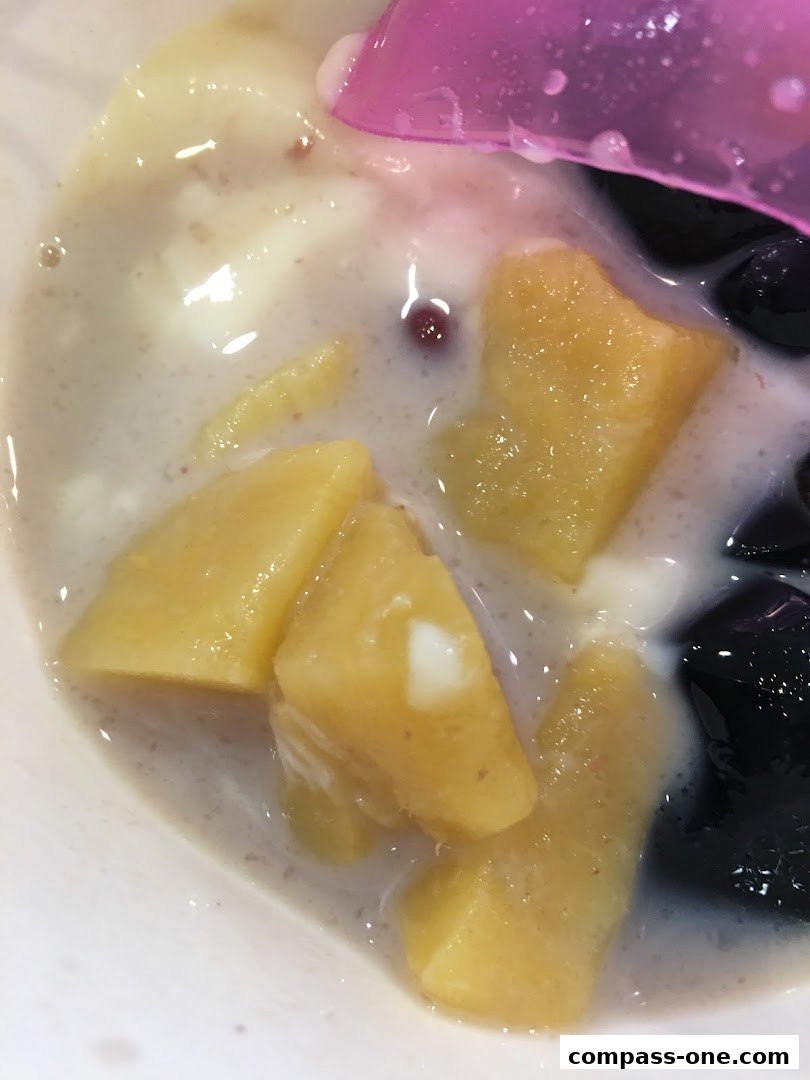 A close-up of a refreshing dessert with mango chunks, grass jelly, and a creamy base.