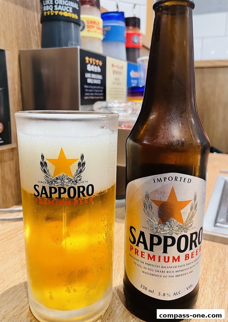 A glass of Sapporo Premium Beer next to a bottle of the same beer, with sauces in the background.