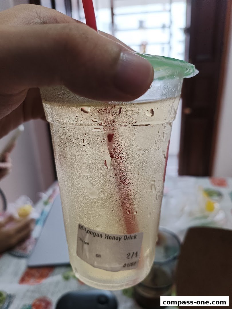 A hand holds a cold, sweating cup of Gong Cha's Longan Honey Drink.