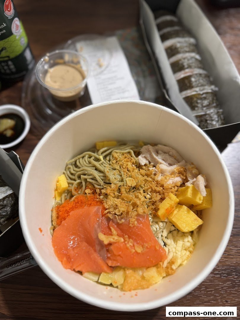 A close-up of a delicious salmon poke bowl with noodles, toppings, and a side of sushi rolls.
