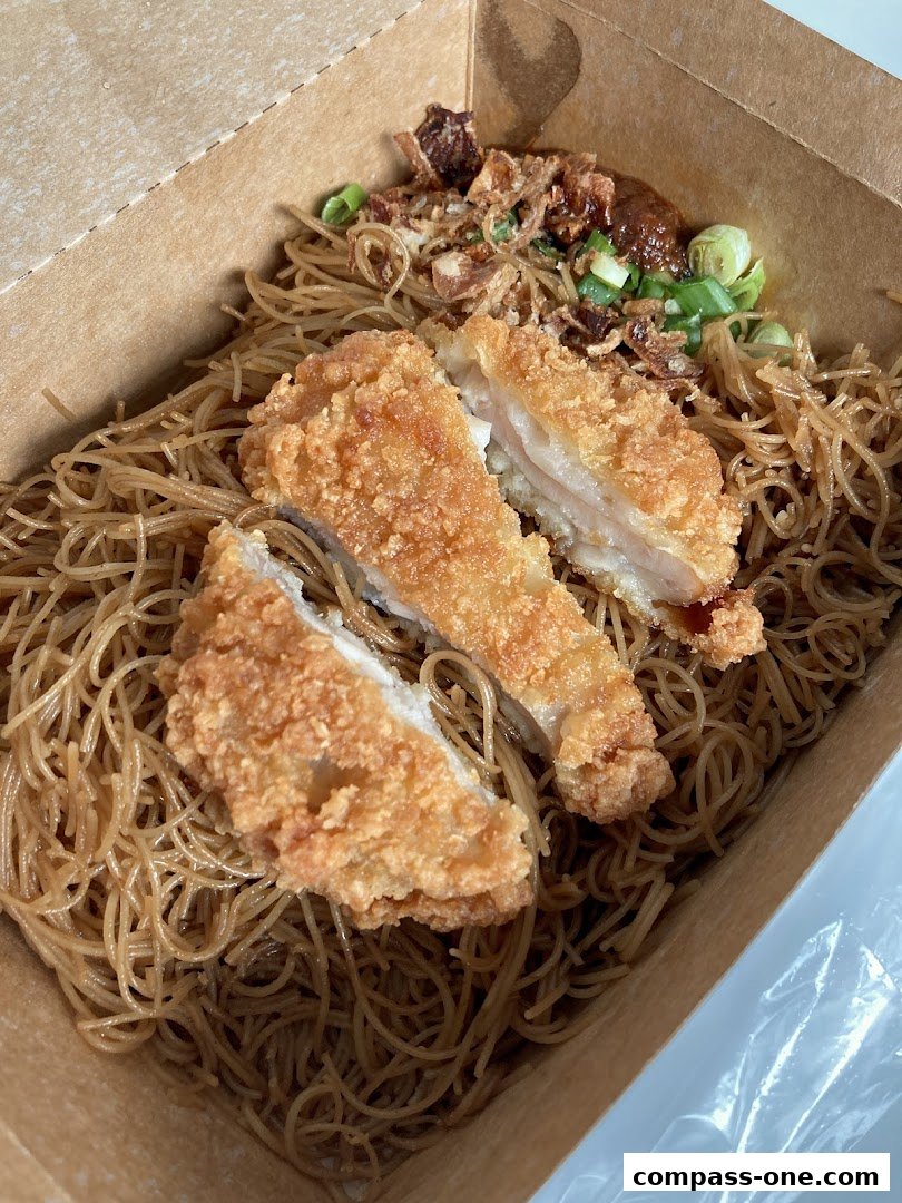 A takeaway box filled with noodles and crispy fried chicken.