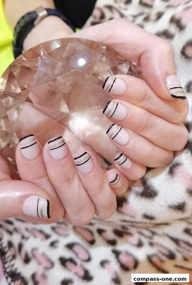 Close-up of hands with stylish light pink nails featuring black and gold stripe accents.
