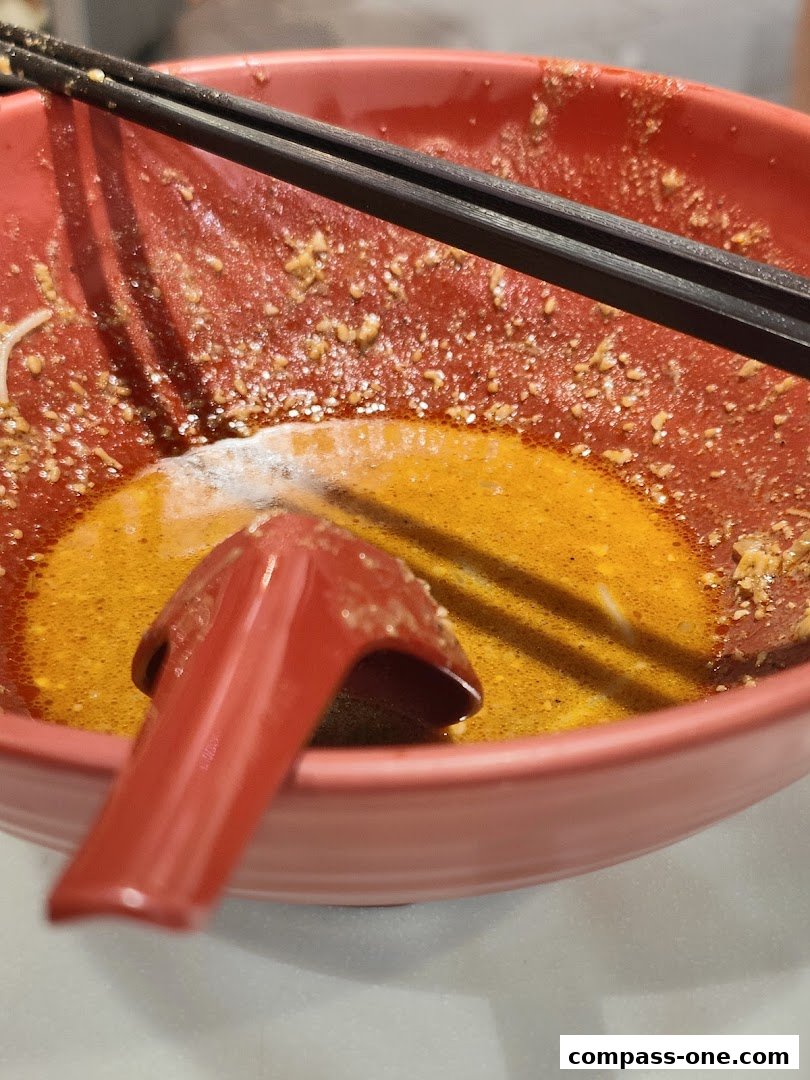 A close-up of a nearly empty bowl of ramen with chopsticks and a spoon.