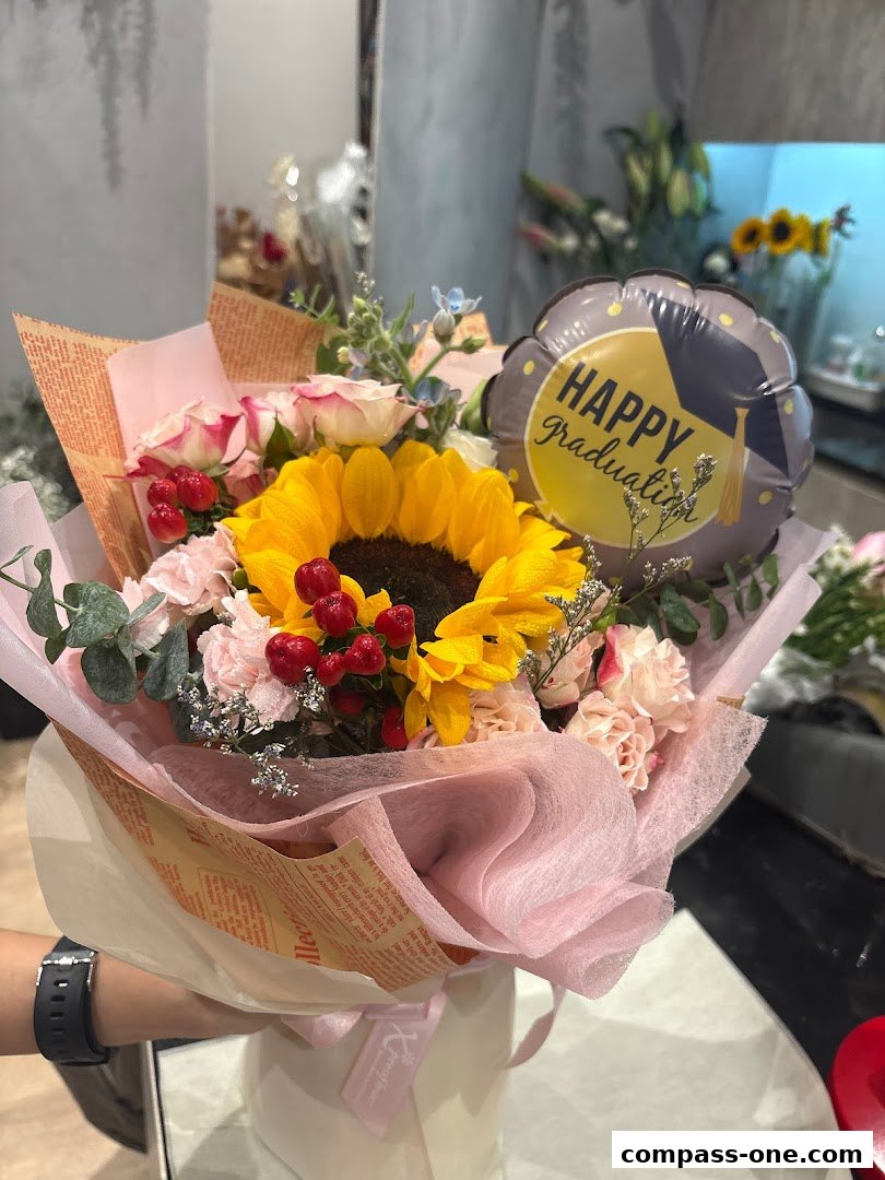 A hand holds a graduation-themed flower bouquet with a sunflower and roses.