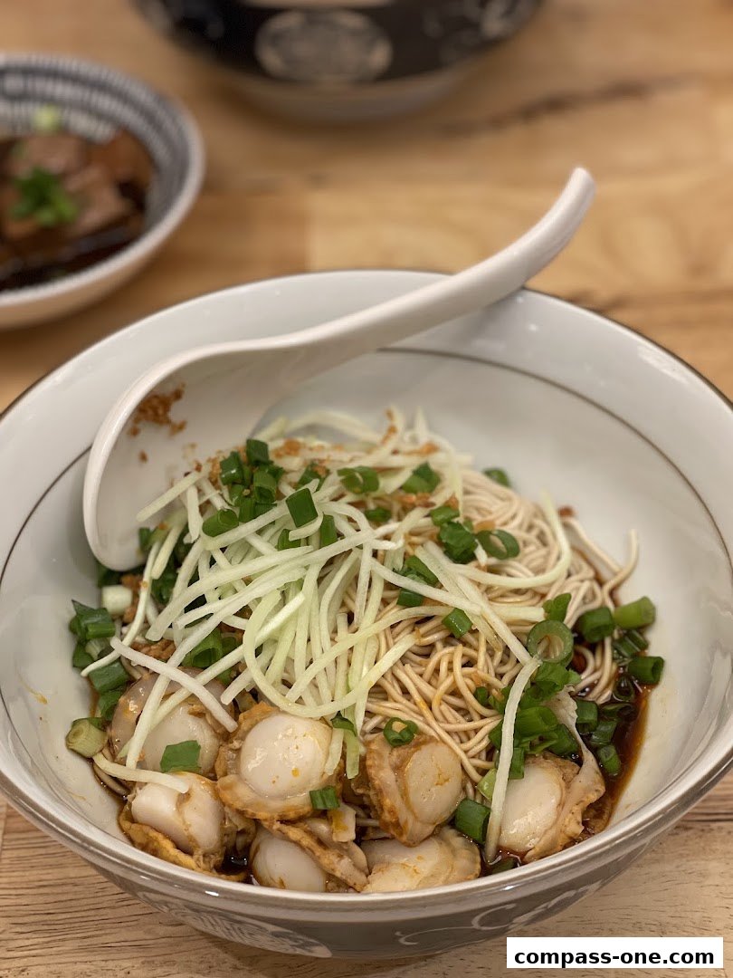 A close-up of a bowl of noodles with scallops, scallions, and shredded cucumber.
