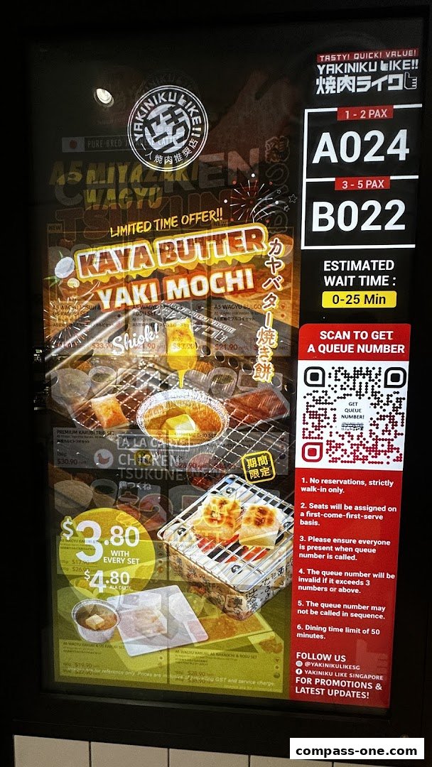 A digital display showing a queue number, estimated wait time, and promotional food items for Yakiniku Like.